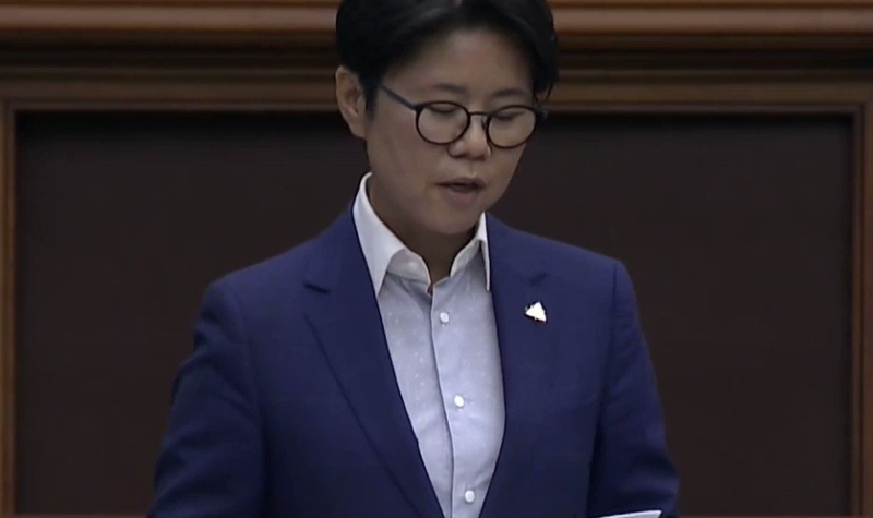 A person in a blue suit and white dress shirt. They are wearing glasses as they read a white paper.