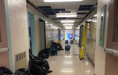 A school hallway filled will trash bags and fans after a flood