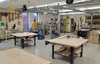 The inside of the tech education shop and classroom at Liverpool Regional High School with four empty wooden worktables and tools in the background