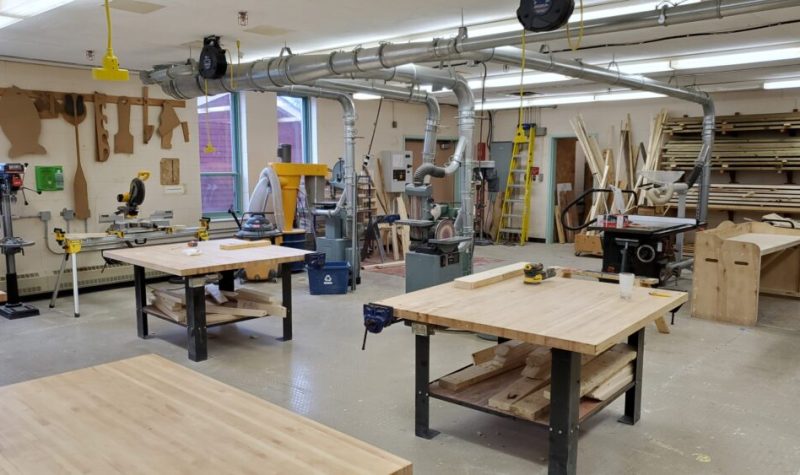 The inside of the tech education shop and classroom at Liverpool Regional High School with four empty wooden worktables and tools in the background