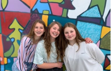 trois filles posent devant un mur coloré