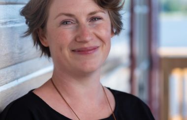 A headshot of a woman leaning against the side of a house