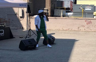 On peut voir le rappeur L Flofranco en prestation dans le stationnement de l'édifice de la Clé de la Baie situé au 63 rue Main à Penetanguishene. Il est devant une tente ou son équipement et placé. Le chanteur porte des vêtements verts et blancs, les couleurs du drapeau franco-ontarien, pour l'occasion.