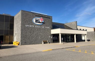 On peut voir la façade du North Simcoe Sport and Recreation Center de Midland. C'est un bâtiment moderne fait de brique et de béton gris. L'affiche du Centre est visible sur la façade