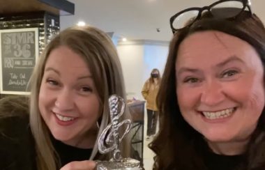 Two women smile, as one of them holds up a trophy.