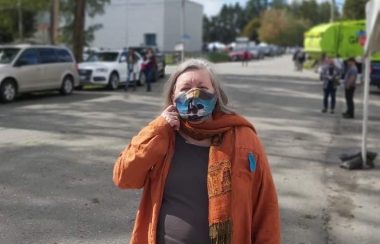Lynn Perrin Holding her mask in front of a busy street