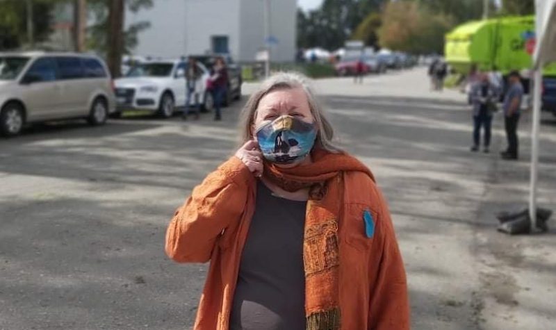 Lynn Perrin Holding her mask in front of a busy street
