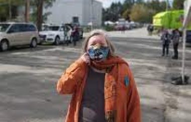 A photo of Lynn Perrin standing outside on a local street wearing a mask