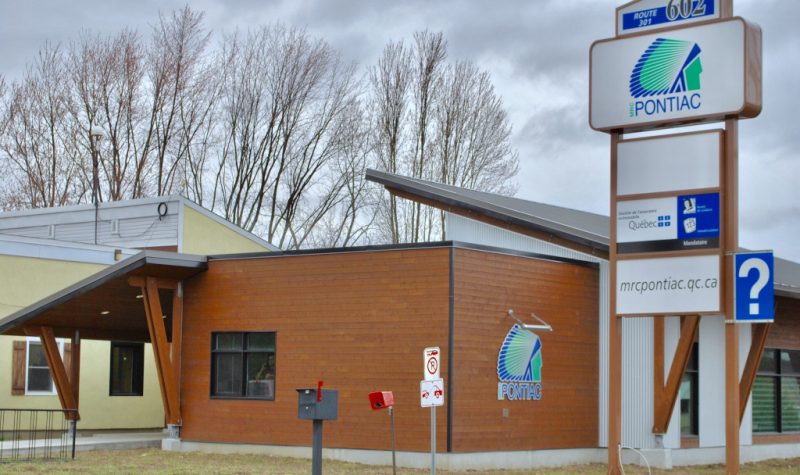 A photo of the exterior of the MRC Pontiac office, featuring brown siding and a large sign with a white background.