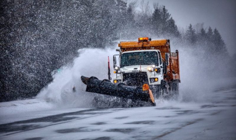 Un camion de déneigement sur la route qui nettoie la chaussée dans une tempête de neige