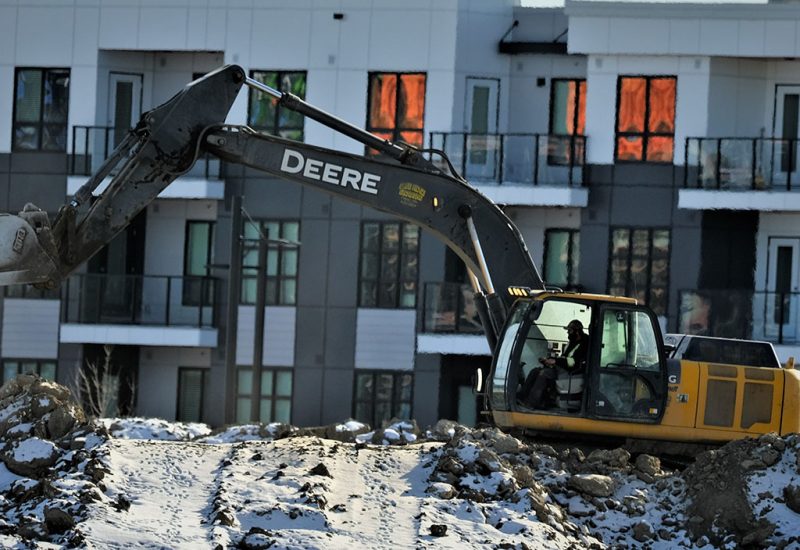 A construction truck digging in front of a townhouse complex.