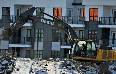 A construction truck digging in front of a townhouse complex.