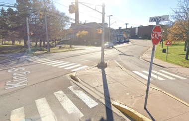 Photo of intersection with white painted zebra stripe crosswalks extending in two directions, for a median. Stop sign and crossing lights showing. Street sign says King Street