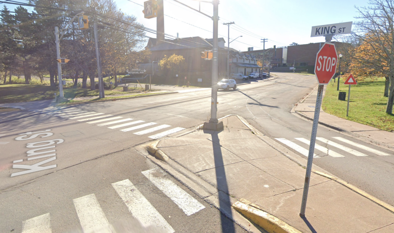 Photo of intersection with white painted zebra stripe crosswalks extending in two directions, for a median. Stop sign and crossing lights showing. Street sign says King Street