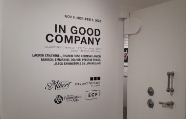 Sign in white background with black lettering, In Good Company, of seven artists work on display in St. Albert