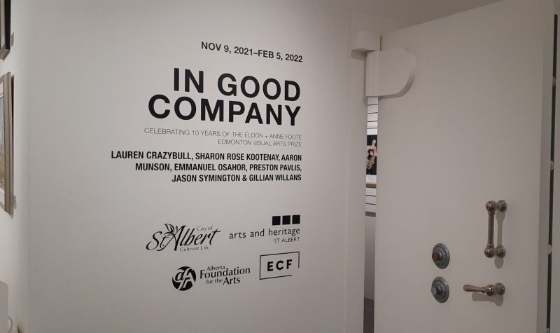 Sign in white background with black lettering, In Good Company, of seven artists work on display in St. Albert