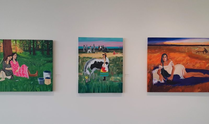 Three bright and vivid art pieces of Lana Whiskeyjack exhibit, first picture is a couple sisters taking a break from berry picking sitting against a tree and second a woman in front of a ceremonial grounds, last picture is an Indigenous lady laying on her side with a orange field with an oxen in background