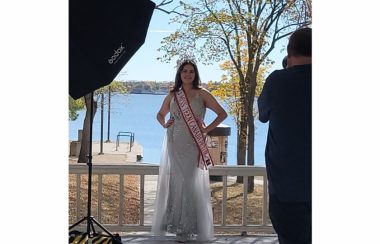 Young indigenous teenage girl wearing a white formal gown and a crown with a sash that reads, Miss Teen Canada Petite 2021-2022