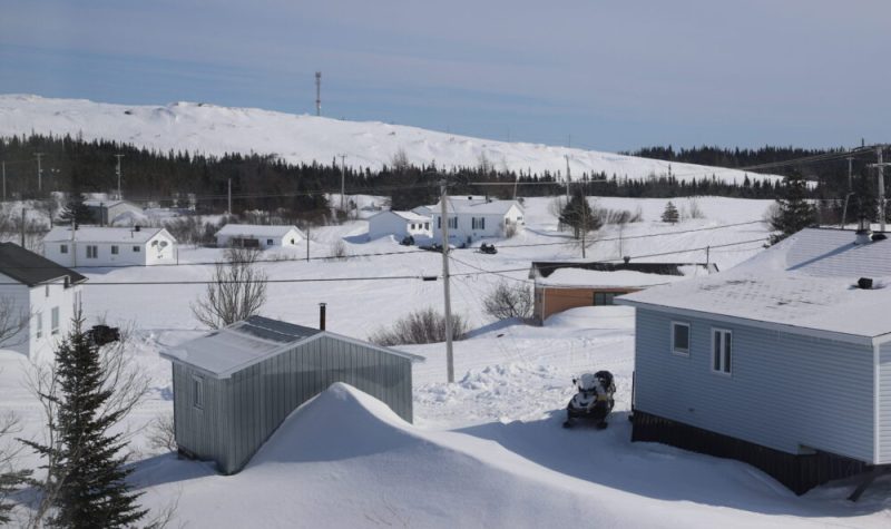 Une dizaine de maisons enneigée se faisant face de part et d'autre d'une rivière gelée. Village québécois.
