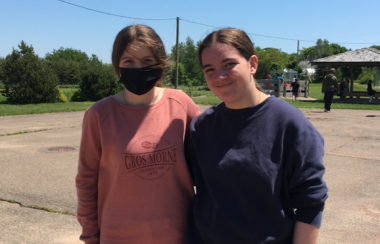 Two young women standing outside in a school yard, one wearing a face mask.