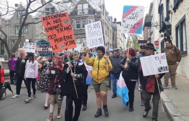 Les manifestants.es brandissent des pancartes colorées. Sur l'une d'entre elles, on peut y lire « Attention à nos enfants trans, c'est peut-être le vôtre ».