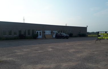 A large one storey brick building with an SUV parked out front and a sign advertising the opening of a retirement residence.