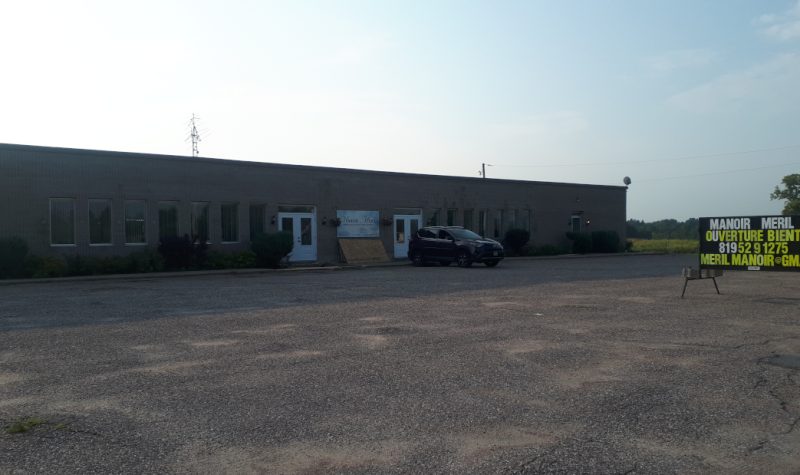 A large one storey brick building with an SUV parked out front and a sign advertising the opening of a retirement residence.