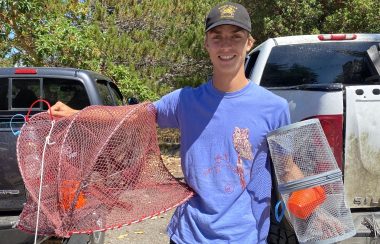 Young man holds up a crab trap and grins.