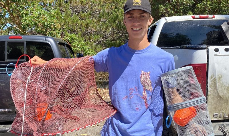 Young man holds up a crab trap and grins.