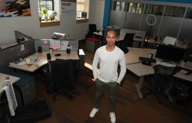 Marc Lafleur, wearing a white shirt and black pants, stands in the centre of his office space.