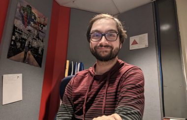 Marc-Samuel assis à son bureau, vêtu d'un pull-over rouge et gris