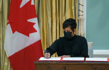 A woman signing a paper with a Canadian flag in the background.