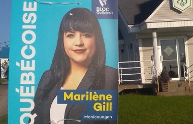 Affiche électorale, avec arrière-plan de couleur bleu poudre, de la candidate bloquiste, Marilène Gill. L'affiche apparaît en face d'une caisse populaire de Tête-à-la-Baleine