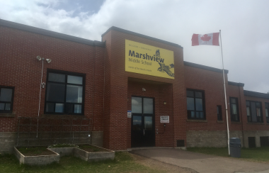 A red brick school building with a yellow sign reading Marshview Middle School, and a flagpole flying Canadian flag in front.