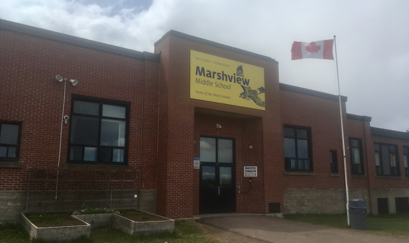 A red brick school building with a yellow sign reading Marshview Middle School, and a flagpole flying Canadian flag in front.