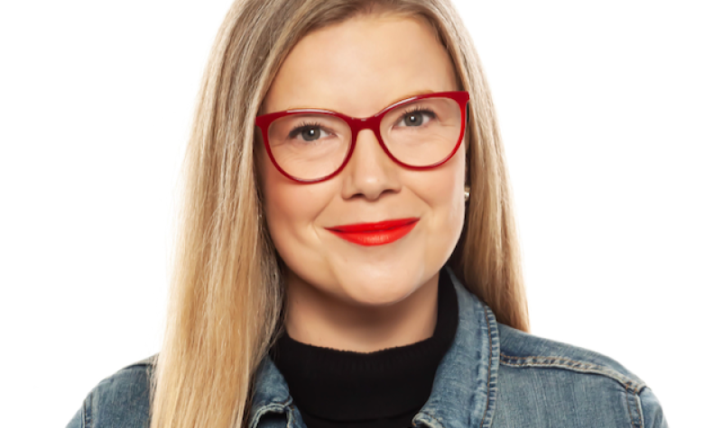 A portrait of a woman with red glasses, smiling at the camera.