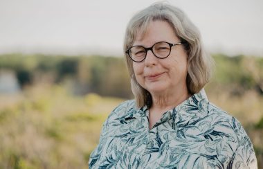 Woman in glasses smiling with grassy field behind her in blur