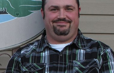 A headshot of Maurice Beauregard in front of a building wearing a plaid shirt.