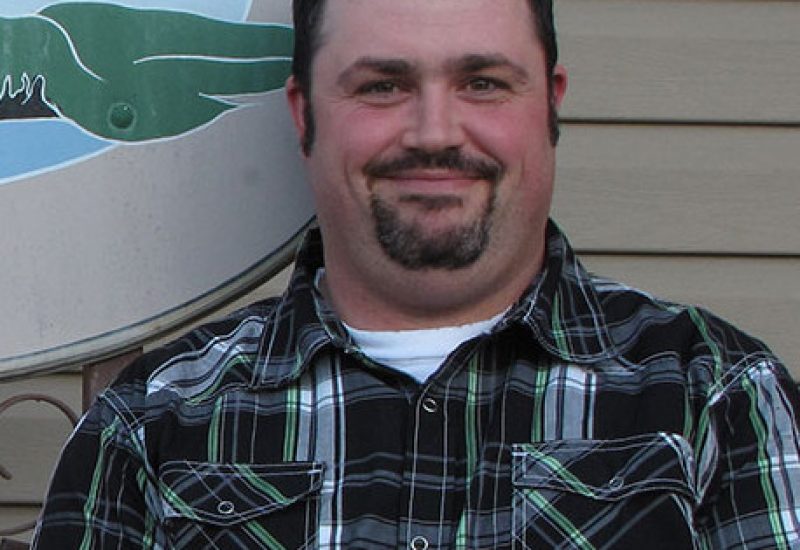 A headshot of Maurice Beauregard in front of a building wearing a plaid shirt.