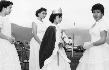 3 women in white dresses stand around a young girl in a crown