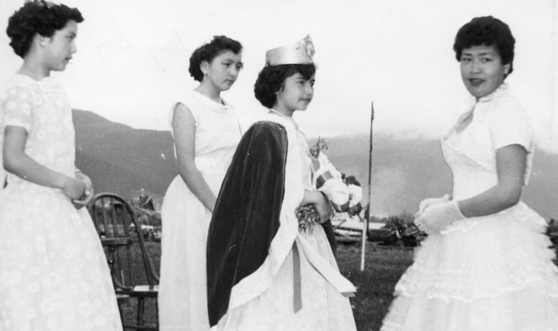 3 women in white dresses stand around a young girl in a crown