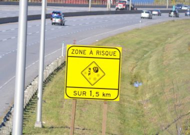 Une affiche jaune indiquant zone à risque dans 1,5 km affichant un pictogramme de vent qui souffle la neige. L'affiche est installé en bordure de l'autoroute 15