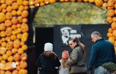 On aperçoit une famille marchant vers « l’arche de citrouille » du parcours « Pumpkinferno » à Penetanguishene. D'autres éléments décoratifs d'Halloween sont visibles sur la photo