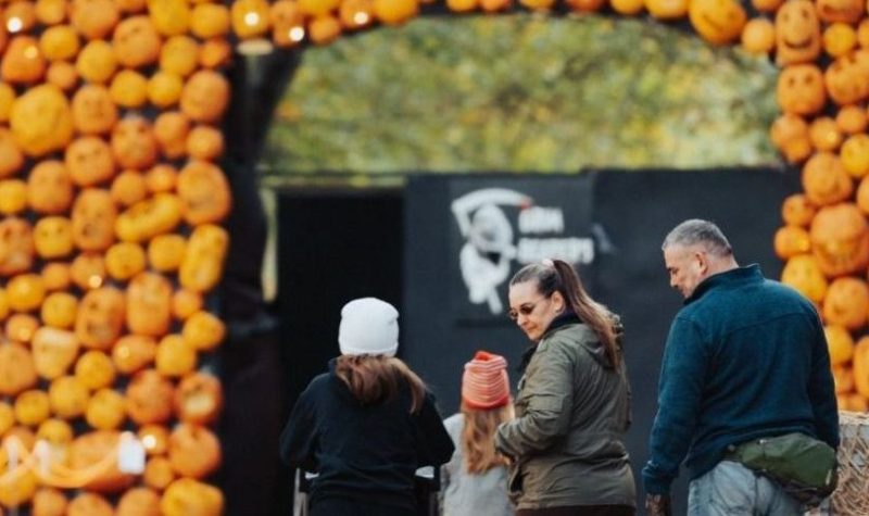 On aperçoit une famille marchant vers « l’arche de citrouille » du parcours « Pumpkinferno » à Penetanguishene. D'autres éléments décoratifs d'Halloween sont visibles sur la photo