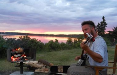 A man places the banjo with a naturscape and sunset in the background.