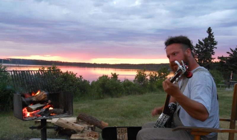 A man places the banjo with a naturscape and sunset in the background.