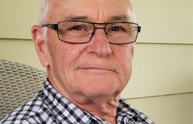 A headshot of Mike McCrank, wearing a black and white plaid shirt and glasses.