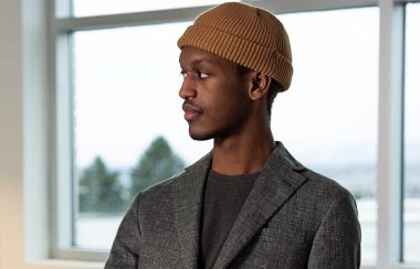 A profile shot of Mike Owen Sebagenzi ,wearing a grey blazer and a beige tuque.