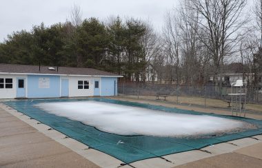 A snow covered pool is seen with a blue building behind it on an overcast winter day in Nova Scotia