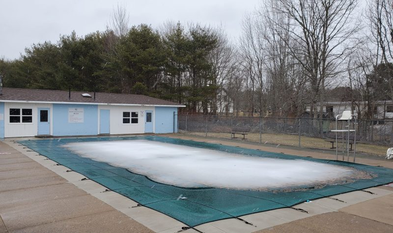 A snow covered pool is seen with a blue building behind it on an overcast winter day in Nova Scotia